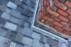 A closeup image of a blue shingled roof with a chimney and flashing.